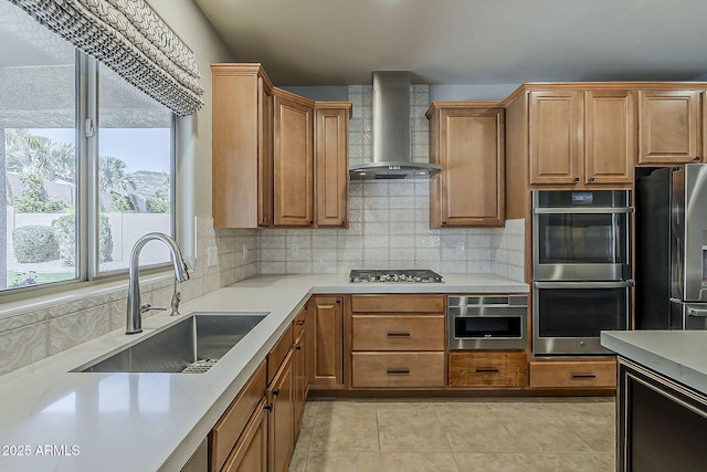 kitchen featuring wall chimney range hood, backsplash, a sink, and stainless steel appliances
