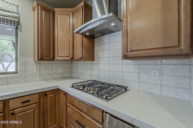 kitchen with decorative backsplash, stainless steel gas cooktop, brown cabinets, and wall chimney exhaust hood