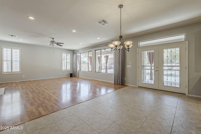 empty room with light tile patterned flooring, ceiling fan with notable chandelier, visible vents, and french doors