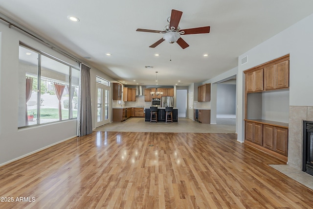 unfurnished living room featuring ceiling fan with notable chandelier, a fireplace, light wood-style floors, and recessed lighting