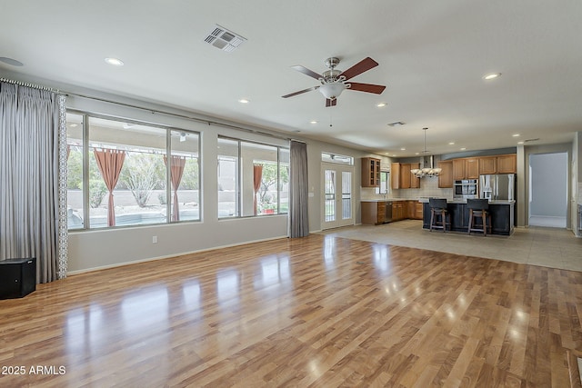 unfurnished living room featuring light wood finished floors, baseboards, ceiling fan with notable chandelier, visible vents, and recessed lighting