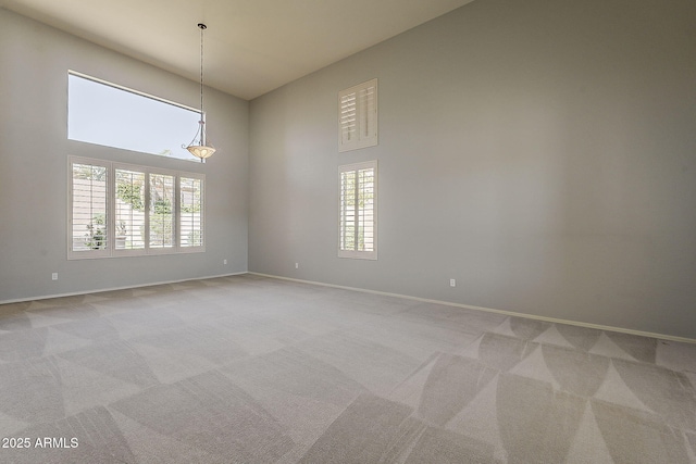 empty room featuring light carpet, baseboards, and a towering ceiling