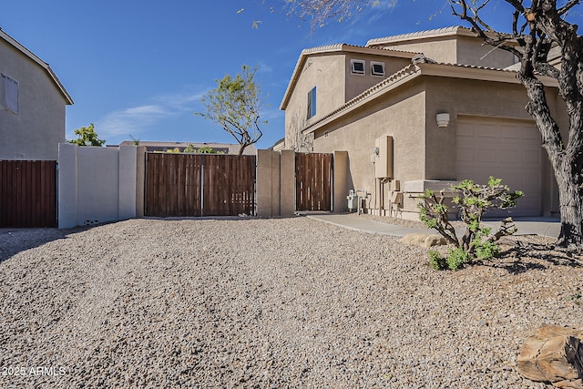 view of property exterior with stucco siding, a gate, a garage, and a tile roof