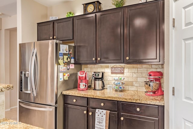 kitchen with stainless steel refrigerator with ice dispenser, dark brown cabinets, decorative backsplash, light stone countertops, and tile patterned flooring