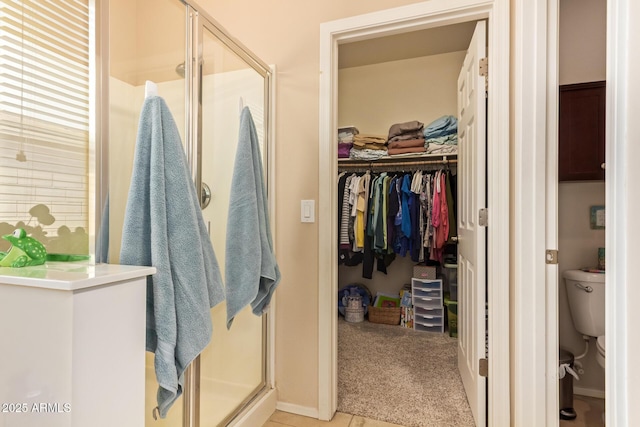 full bathroom featuring a stall shower, a walk in closet, toilet, and baseboards