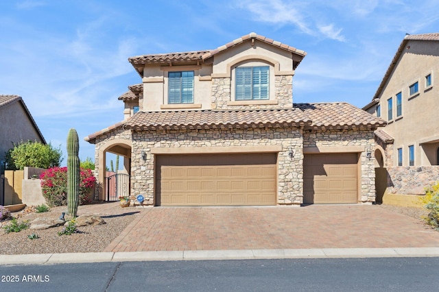 mediterranean / spanish-style home featuring stone siding, decorative driveway, a tile roof, and a gate