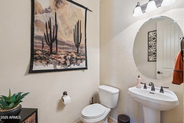 half bath with baseboards, a sink, and toilet