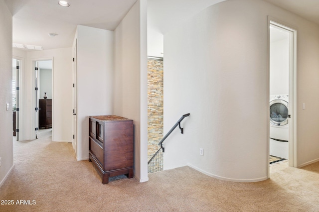 hallway featuring washer / dryer, baseboards, light colored carpet, and an upstairs landing