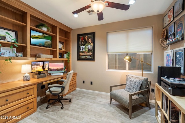 office space with a ceiling fan, visible vents, baseboards, light wood finished floors, and built in desk