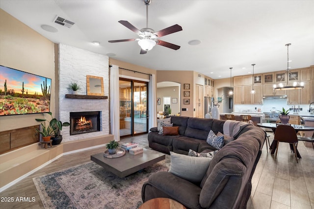 living room featuring arched walkways, a fireplace, visible vents, a ceiling fan, and light wood-type flooring