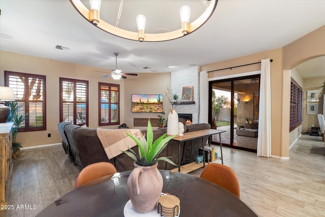 dining room with visible vents, arched walkways, a ceiling fan, light wood-type flooring, and a fireplace