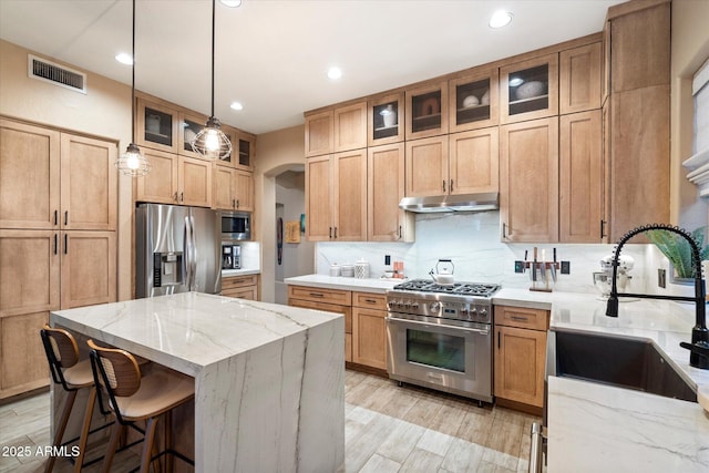 kitchen with arched walkways, under cabinet range hood, a sink, appliances with stainless steel finishes, and a center island