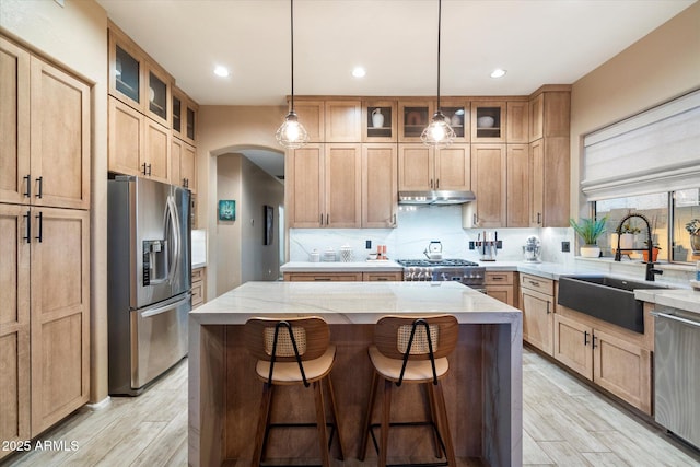 kitchen with arched walkways, a sink, appliances with stainless steel finishes, a center island, and tasteful backsplash