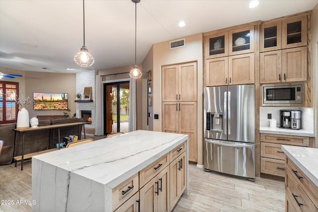 kitchen with pendant lighting, a fireplace, visible vents, appliances with stainless steel finishes, and light stone countertops