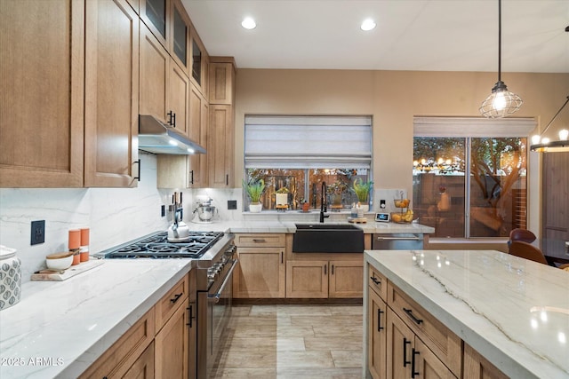 kitchen featuring light stone counters, stainless steel range, tasteful backsplash, a sink, and under cabinet range hood