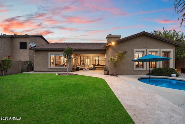 back of property at dusk featuring a yard, stucco siding, an outdoor hangout area, a patio area, and fence