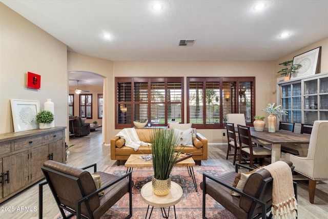 living area with light wood-style flooring, visible vents, arched walkways, and a wealth of natural light