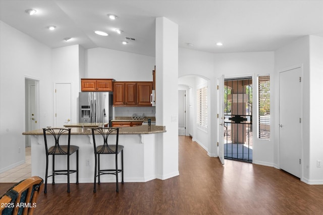 4976 S Sugarberry Ln, Gilbert, AZ 85298 - kitchen with stainless steel fridge, arched walkways, brown cabinetry, a breakfast bar, and a peninsula