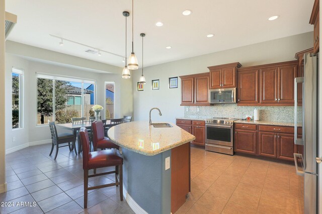 kitchen featuring appliances with stainless steel finishes, light stone counters, sink, a center island with sink, and a breakfast bar area