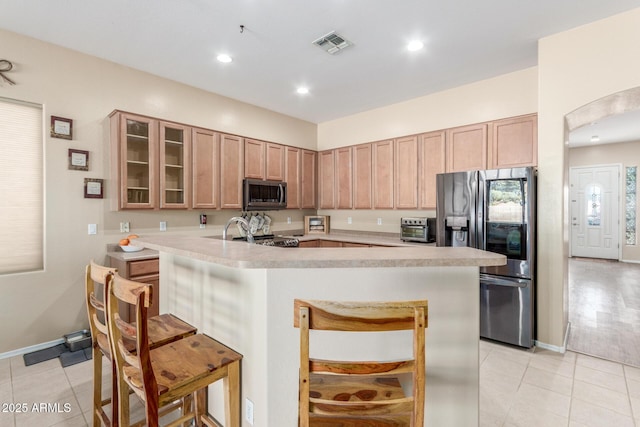 kitchen featuring a kitchen breakfast bar, a kitchen island with sink, light tile patterned floors, and appliances with stainless steel finishes