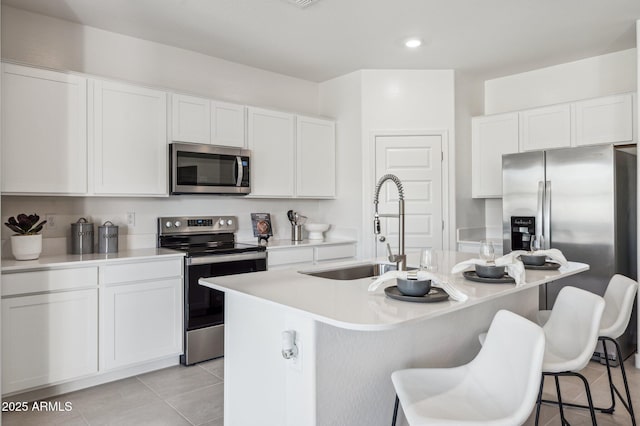 1584 S 241st Ave, Buckeye, AZ 85326 - kitchen with stainless steel appliances, an island with sink, a breakfast bar, light tile patterned floors, and light countertops