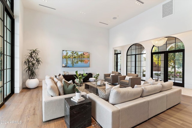 living area featuring french doors, light wood-type flooring, a towering ceiling, and visible vents