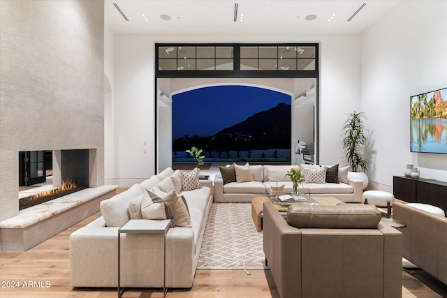 living area featuring light wood-style floors, a warm lit fireplace, visible vents, and a high ceiling