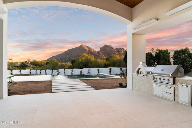 patio terrace at dusk featuring a mountain view, an outdoor kitchen, and area for grilling