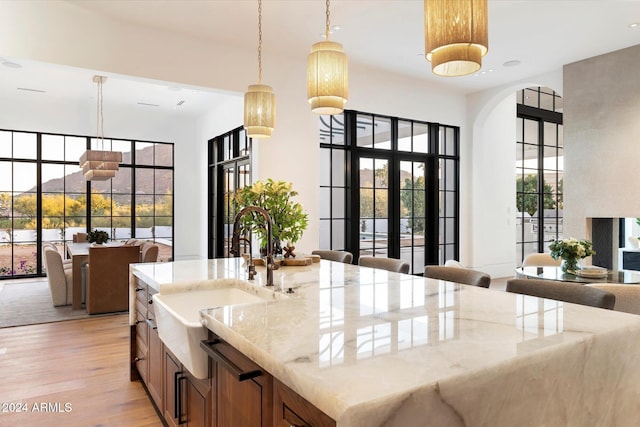 kitchen featuring light stone counters, hanging light fixtures, light wood-style flooring, open floor plan, and a sink