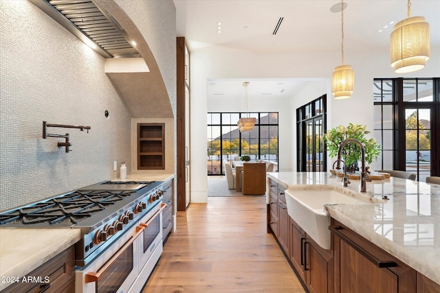 kitchen with light wood finished floors, tasteful backsplash, range with two ovens, pendant lighting, and a sink