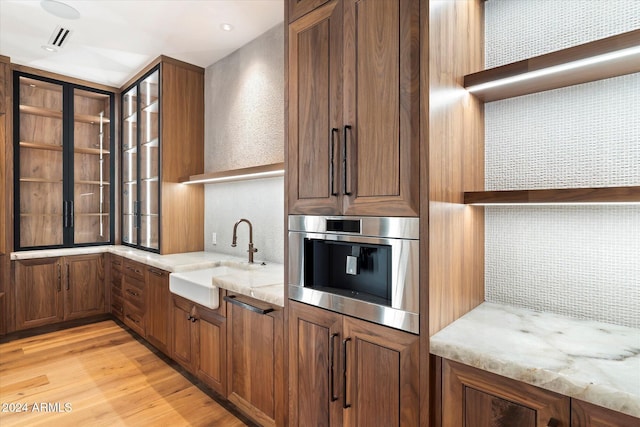 kitchen featuring backsplash, light stone counters, sink, and light hardwood / wood-style flooring