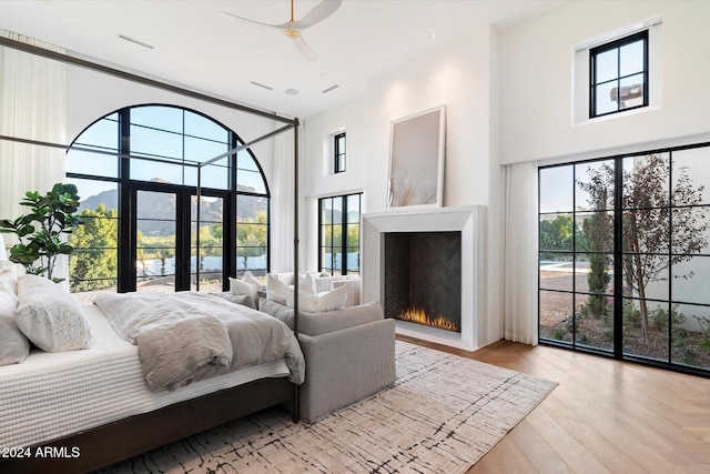 bedroom featuring visible vents, a ceiling fan, wood finished floors, a lit fireplace, and a high ceiling