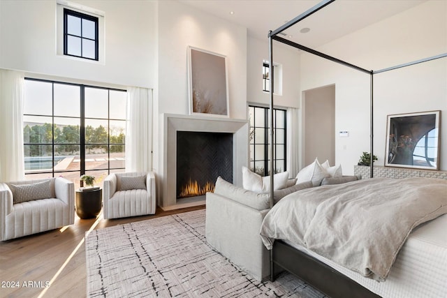 bedroom with a warm lit fireplace, wood finished floors, and a towering ceiling