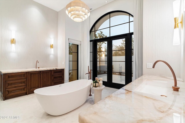 bathroom with french doors, vanity, a tub to relax in, and a notable chandelier