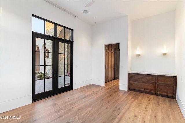 spare room featuring french doors, a towering ceiling, light wood-style flooring, and baseboards