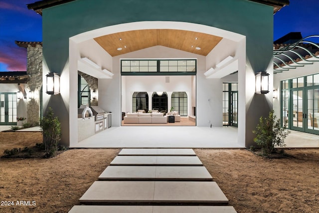 back house at dusk featuring outdoor lounge area, a patio area, french doors, and an outdoor kitchen