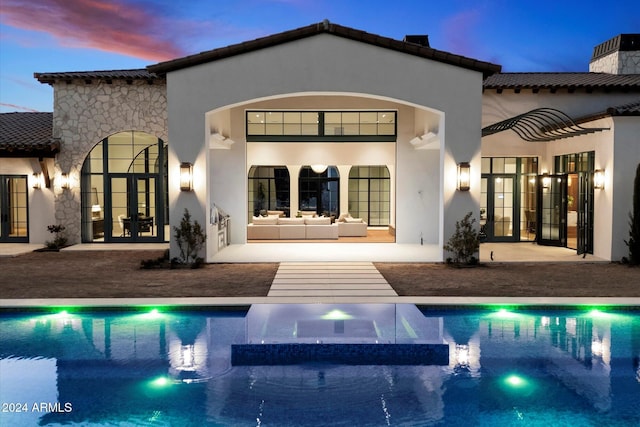 back of house at dusk featuring french doors, a tile roof, a patio, stucco siding, and an outdoor hangout area