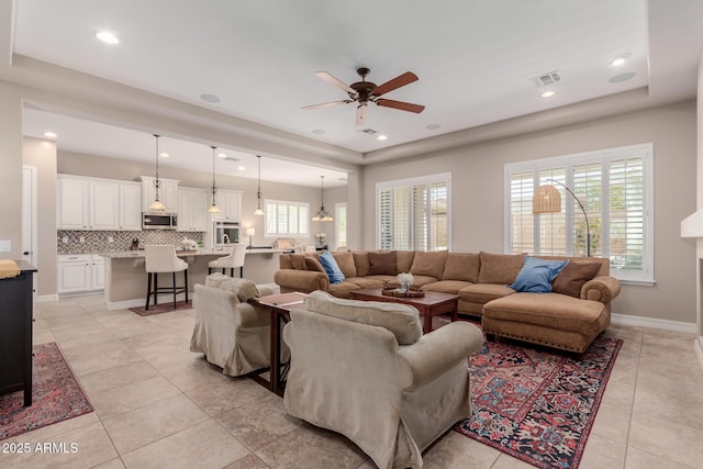 living area featuring light tile patterned floors, visible vents, baseboards, and a ceiling fan