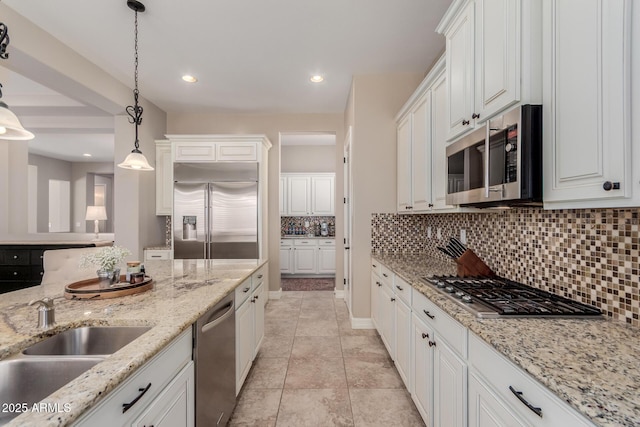 kitchen with a sink, backsplash, stainless steel appliances, white cabinets, and hanging light fixtures