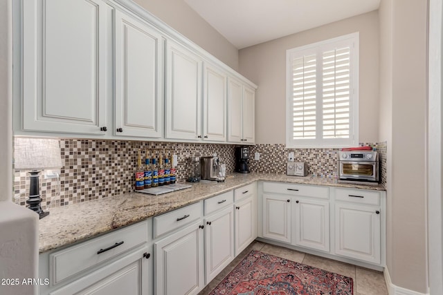 kitchen with light tile patterned flooring, backsplash, white cabinets, and light stone counters