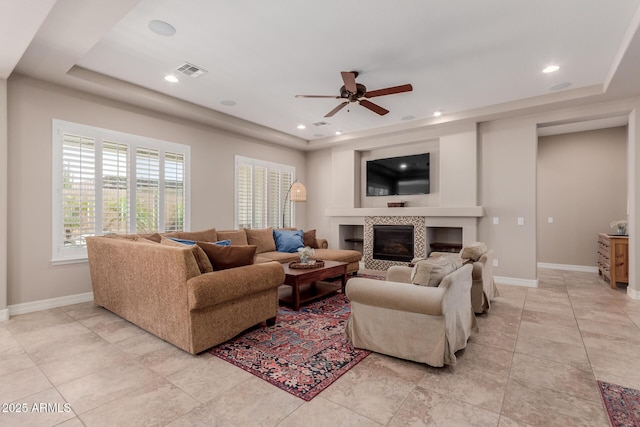 living room featuring visible vents, a ceiling fan, baseboards, a fireplace, and a raised ceiling