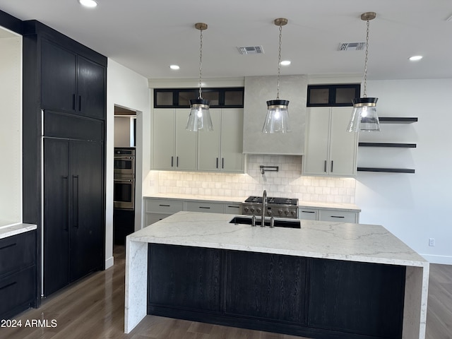 kitchen with light stone counters, sink, white cabinets, and a center island with sink