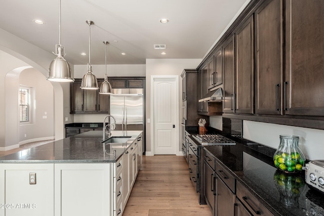 11070 E Bent Tree Dr, Scottsdale, AZ 85262 - kitchen with under cabinet range hood, arched walkways, dark brown cabinetry, a center island with sink, and recessed lighting