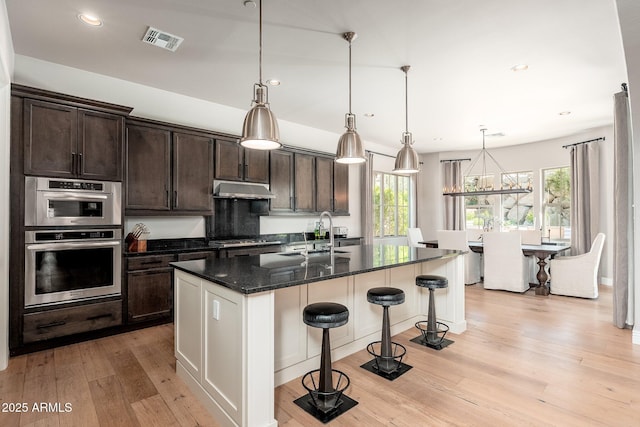 11070 E Bent Tree Dr, Scottsdale, AZ 85262 - kitchen with under cabinet range hood, a breakfast bar area, dark brown cabinetry, light wood-type flooring, and recessed lighting