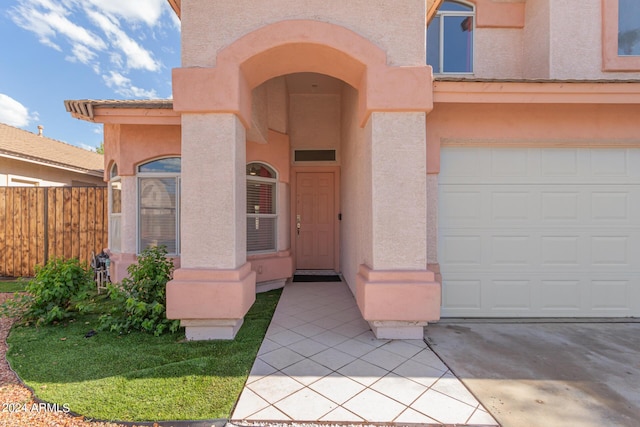 entrance to property featuring a garage, a tile roof, fence, and stucco siding