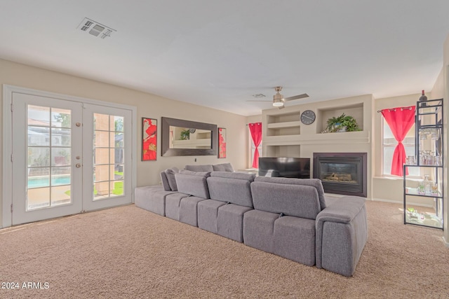 carpeted home theater room featuring a ceiling fan, visible vents, french doors, and a glass covered fireplace