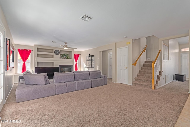 unfurnished living room featuring visible vents, a ceiling fan, a glass covered fireplace, light carpet, and stairs