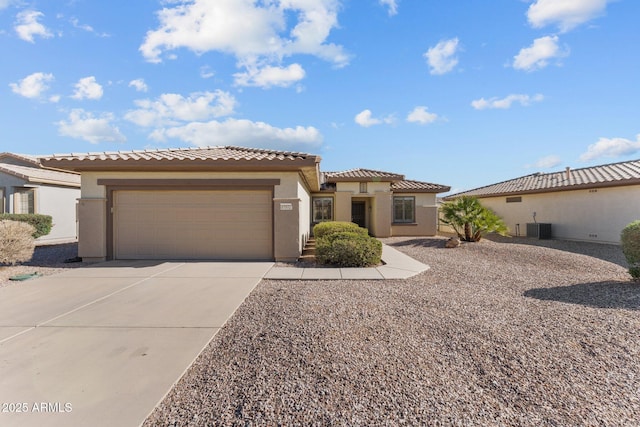 mediterranean / spanish-style home featuring stucco siding, central air condition unit, concrete driveway, an attached garage, and a tiled roof