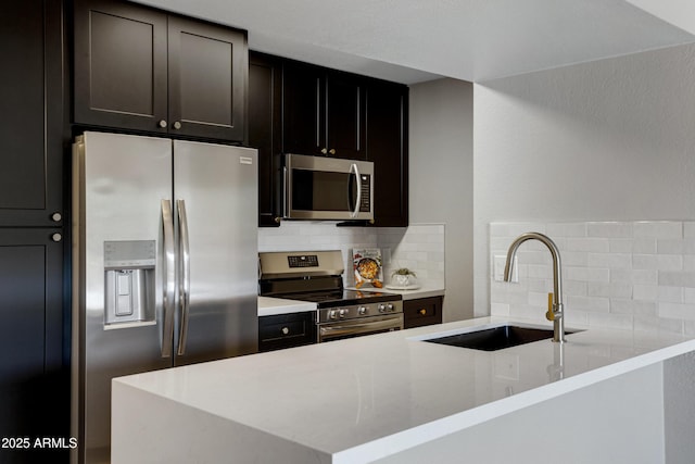 kitchen featuring stainless steel appliances, a sink, backsplash, a peninsula, and light stone countertops