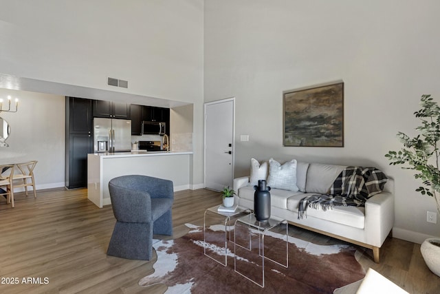 living area with light wood-style floors, a high ceiling, baseboards, and a chandelier